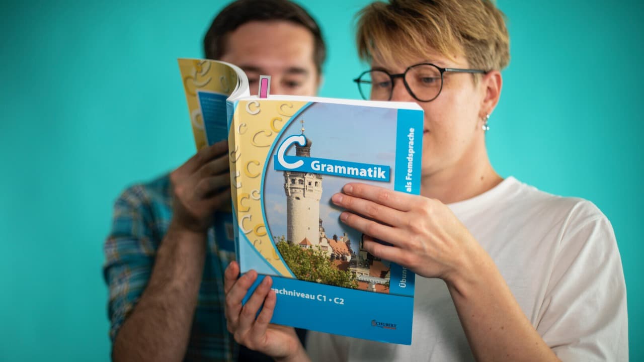 Two language learners holding a C1 German course book